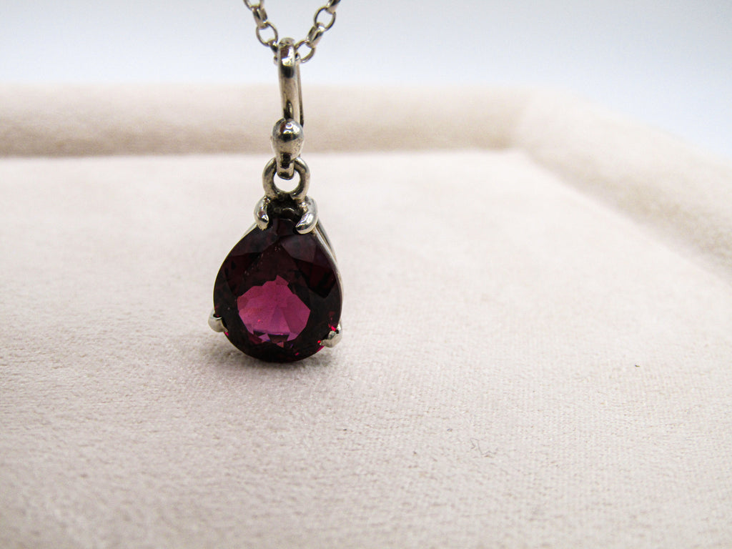 Teardrop-shaped gemstone pendant on a chain against a neutral background