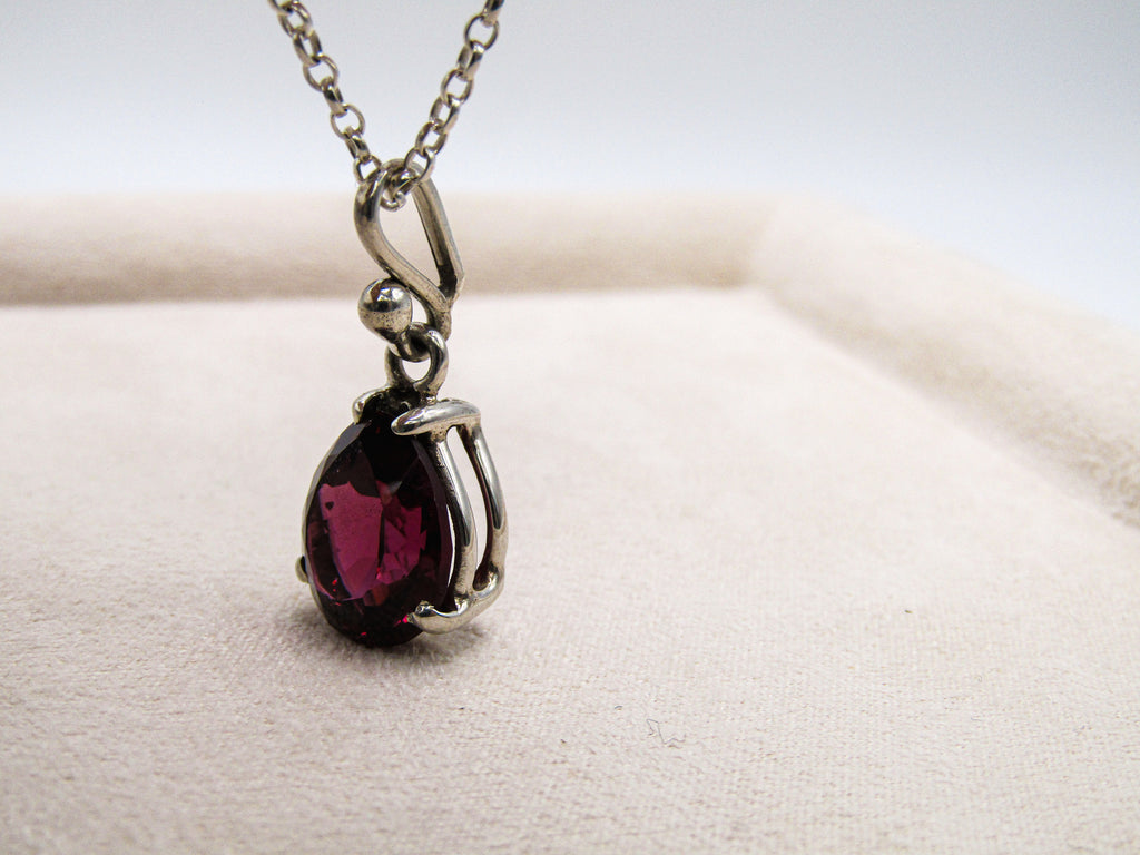 Silver pendant with a red gemstone on a white cushion