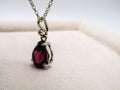 Silver pendant with a red gemstone on a white cushion