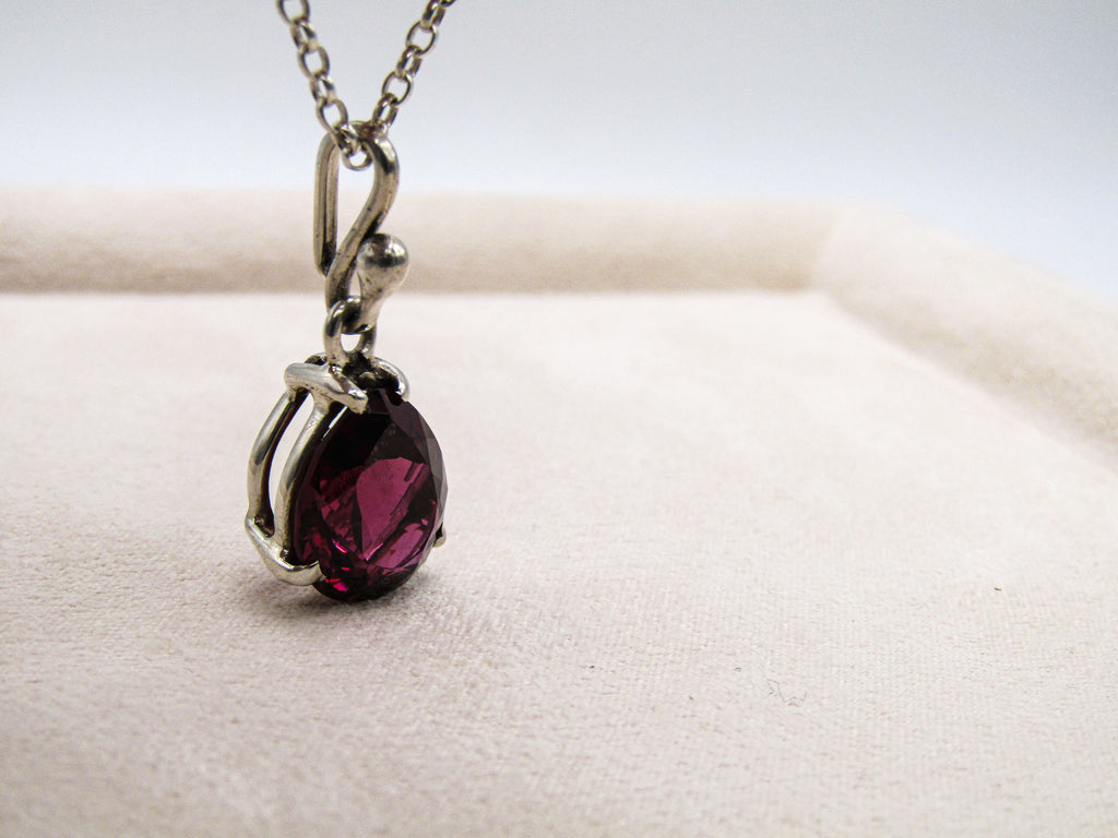 Silver necklace with a red gemstone pendant on a white surface