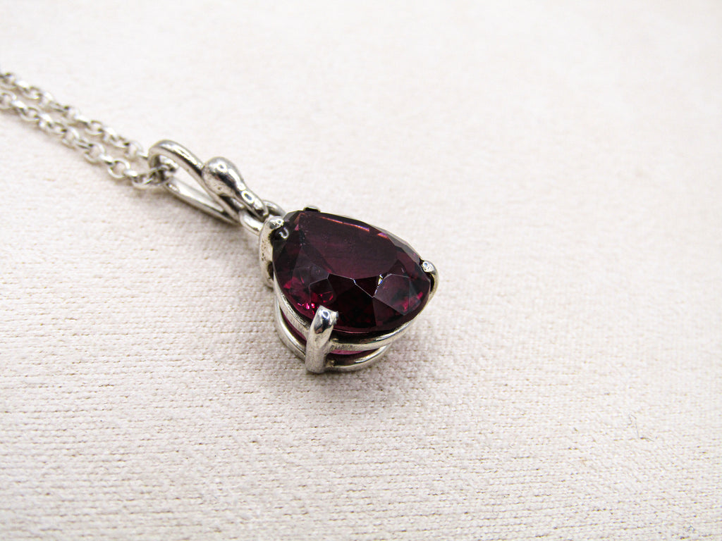 Silver necklace with a red gemstone pendant on a white fabric background