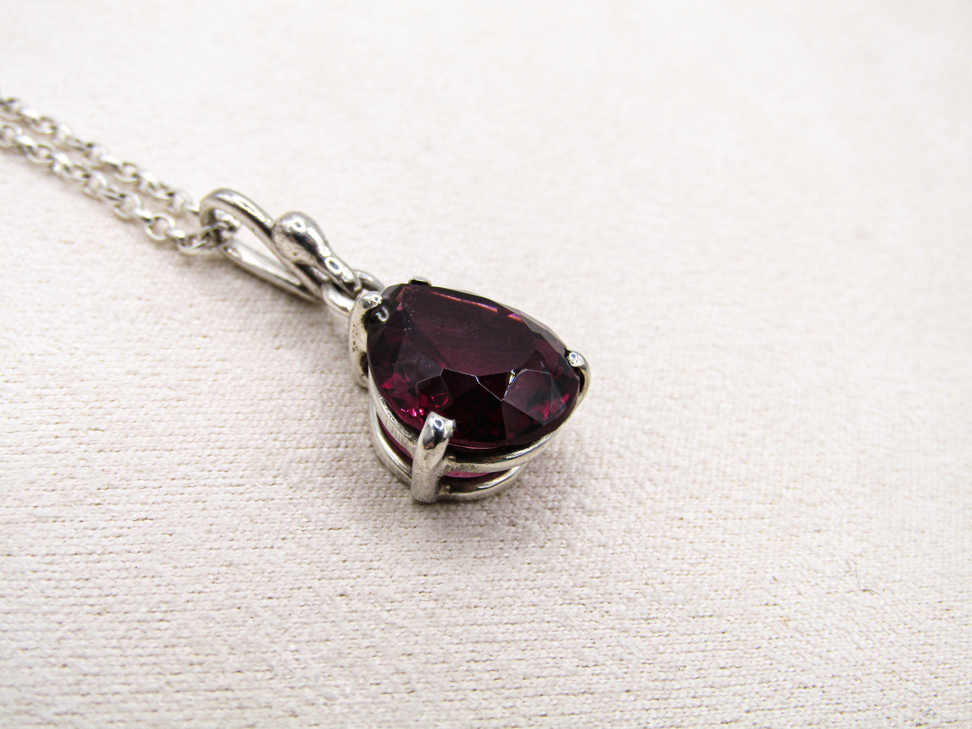 Silver necklace with a red gemstone pendant on a white fabric background