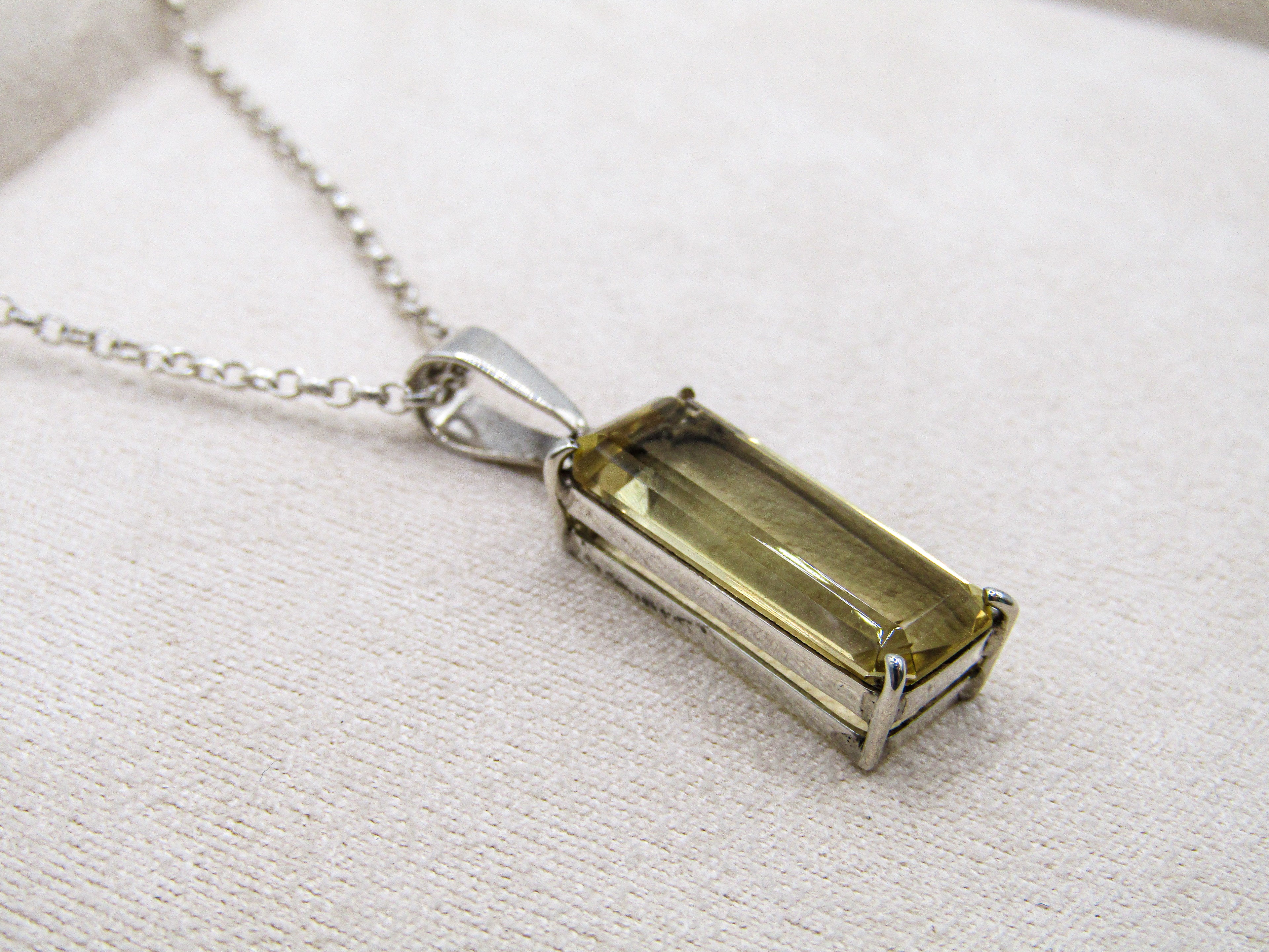 Necklace with a rectangular green gemstone pendant on a light fabric background