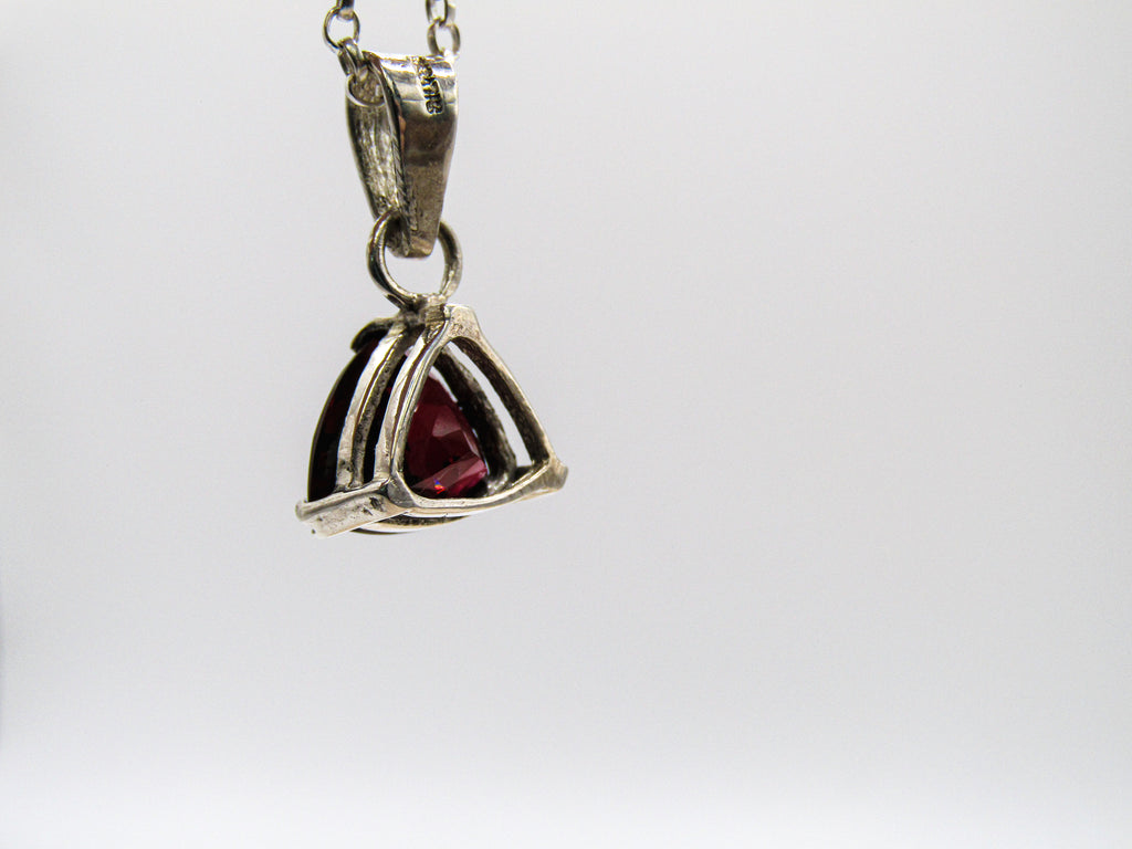 Silver pendant with a red gemstone on a white background