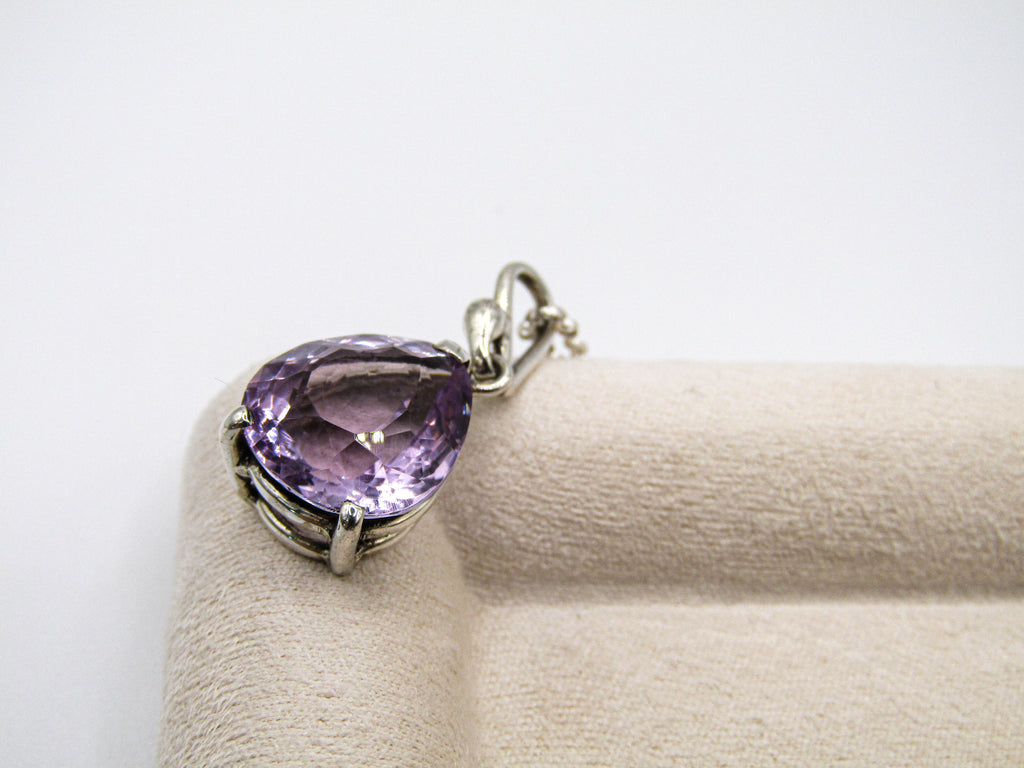 Purple gemstone pendant on a beige cushion with a white background