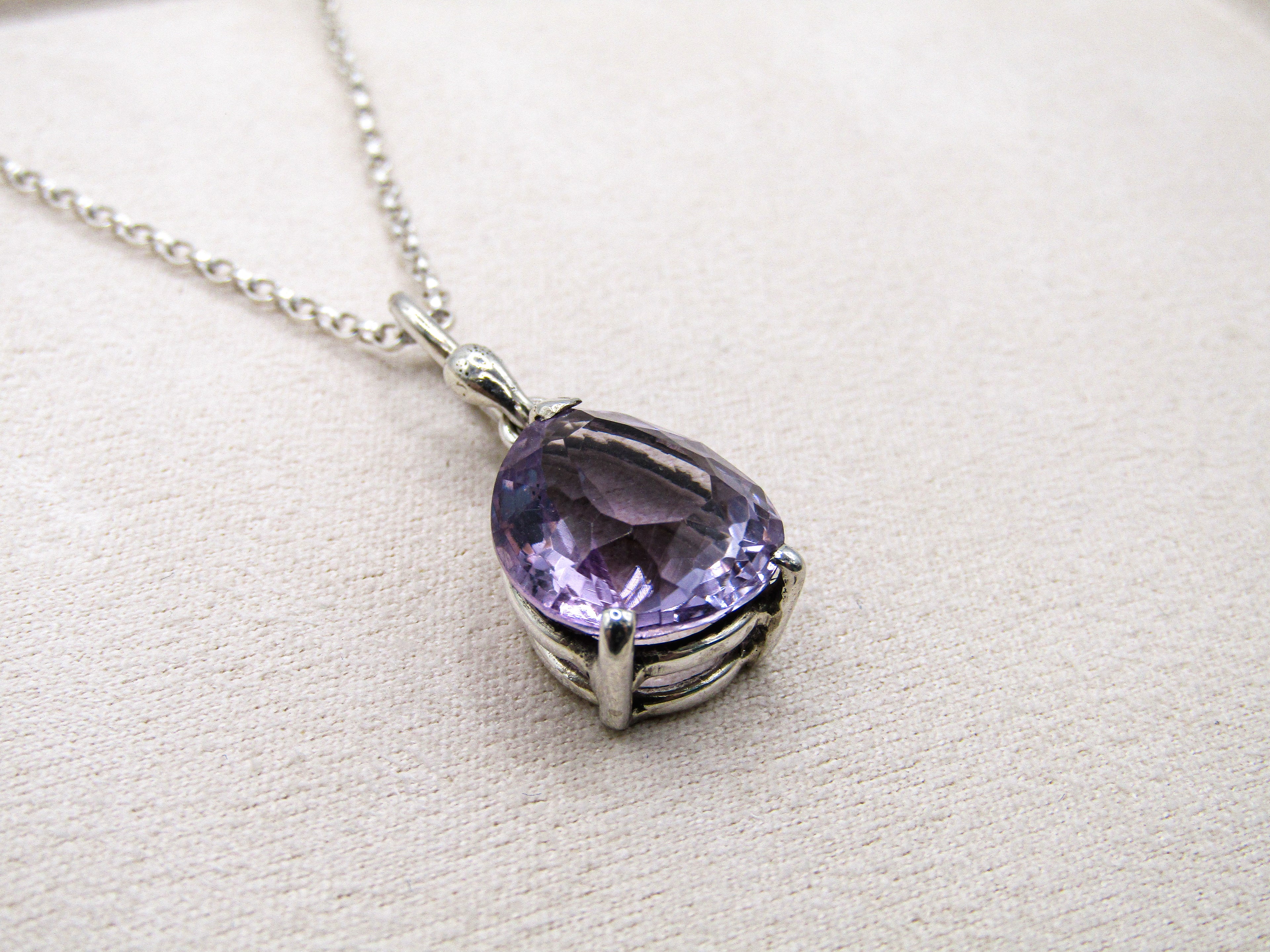 Purple teardrop-shaped gemstone necklace on a light beige background