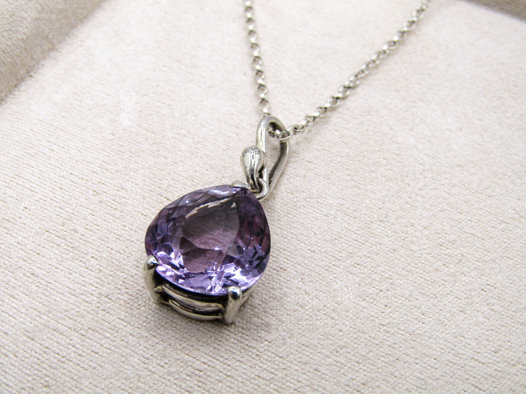 Silver necklace with a purple gemstone pendant on a beige fabric background