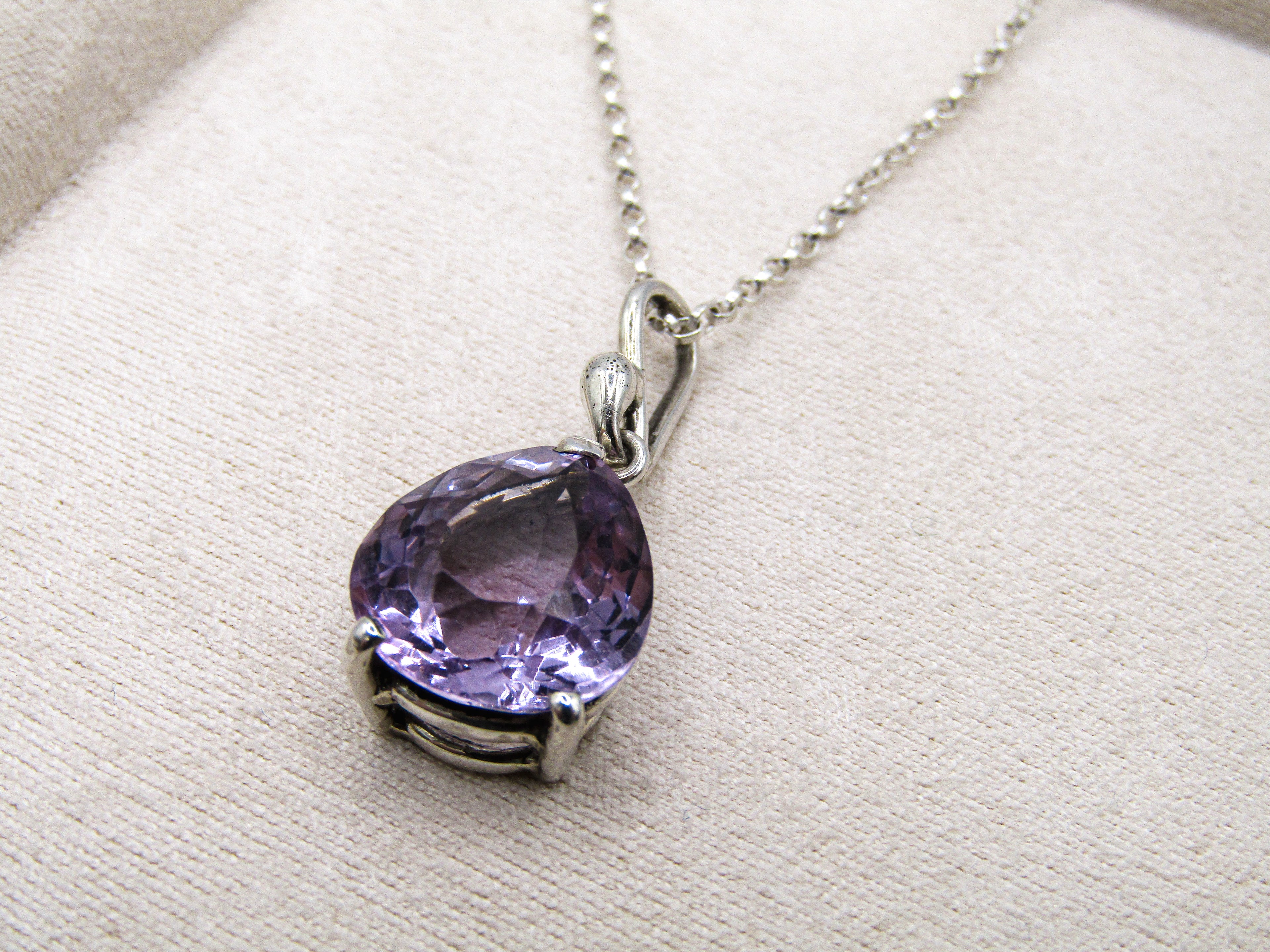 Silver necklace with a purple gemstone pendant on a beige fabric background