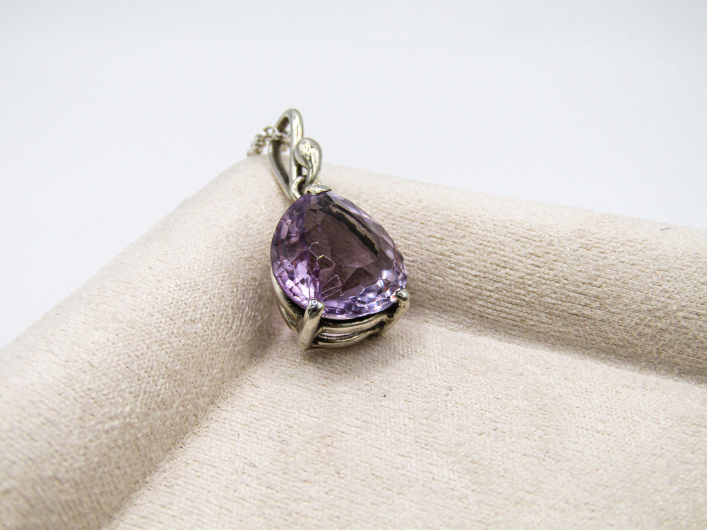 Purple teardrop-shaped gemstone pendant on a beige cushion with a white background