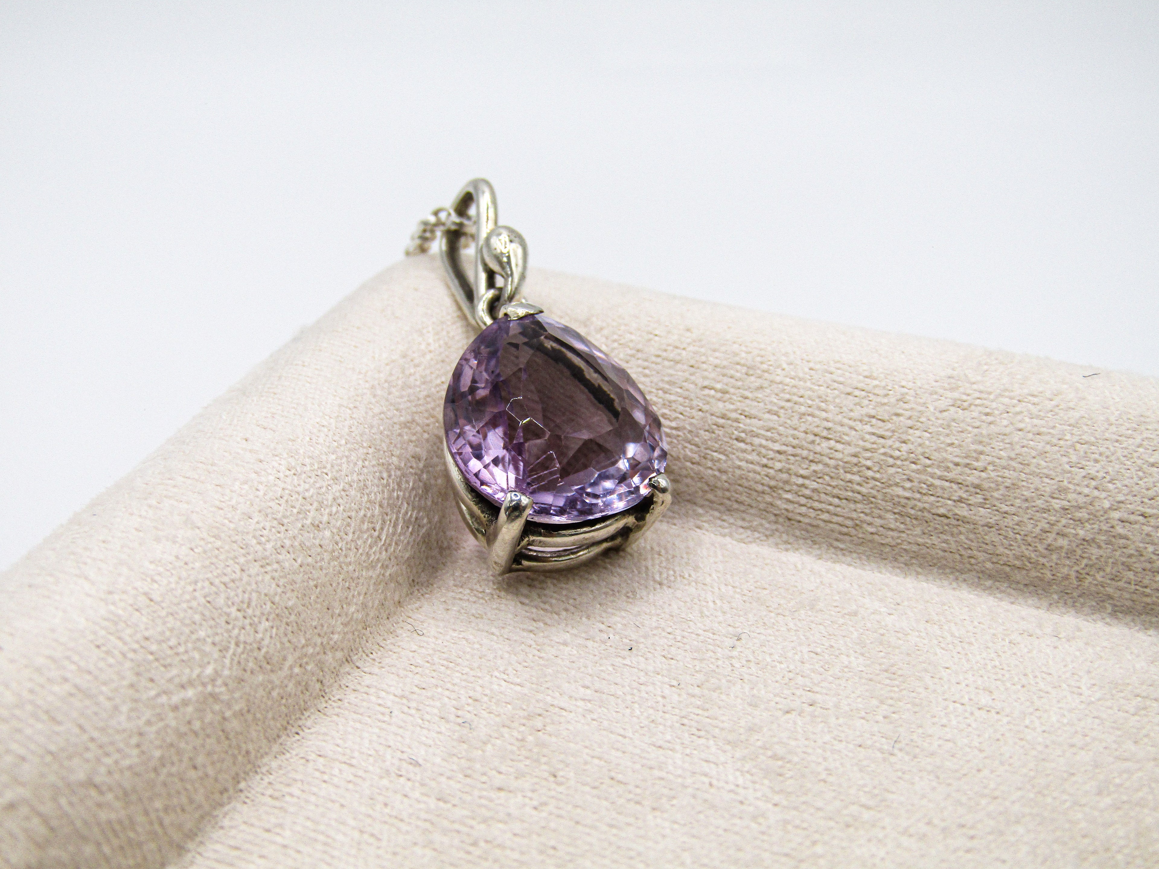 Purple teardrop-shaped gemstone pendant on a beige cushion with a white background
