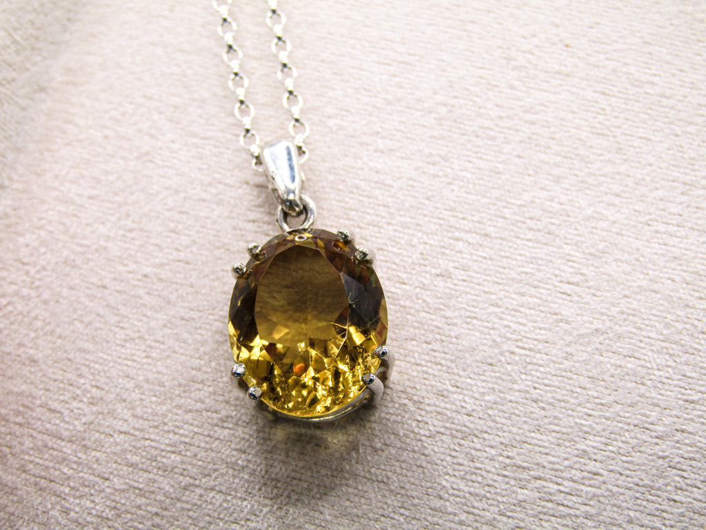 Yellow gemstone pendant on a silver chain against a beige background