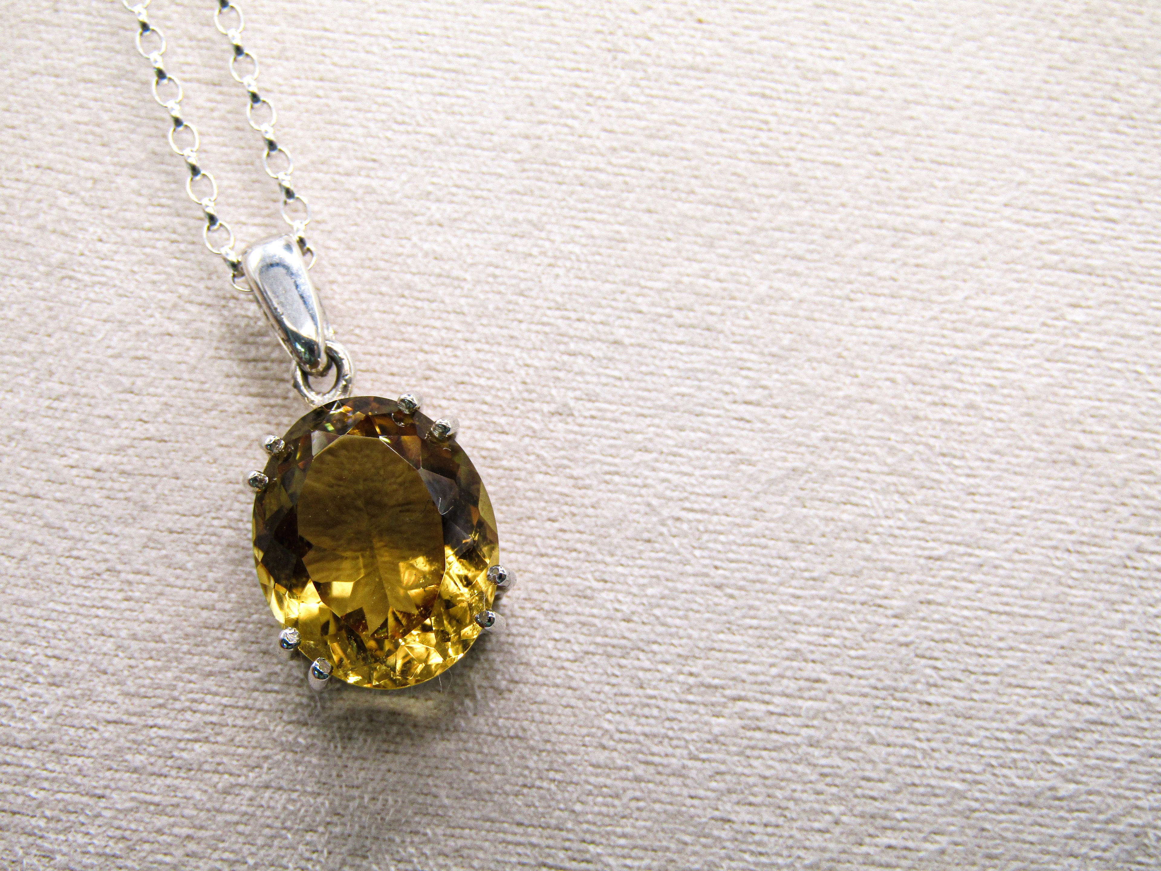 Yellow gemstone pendant on a silver chain against a beige background