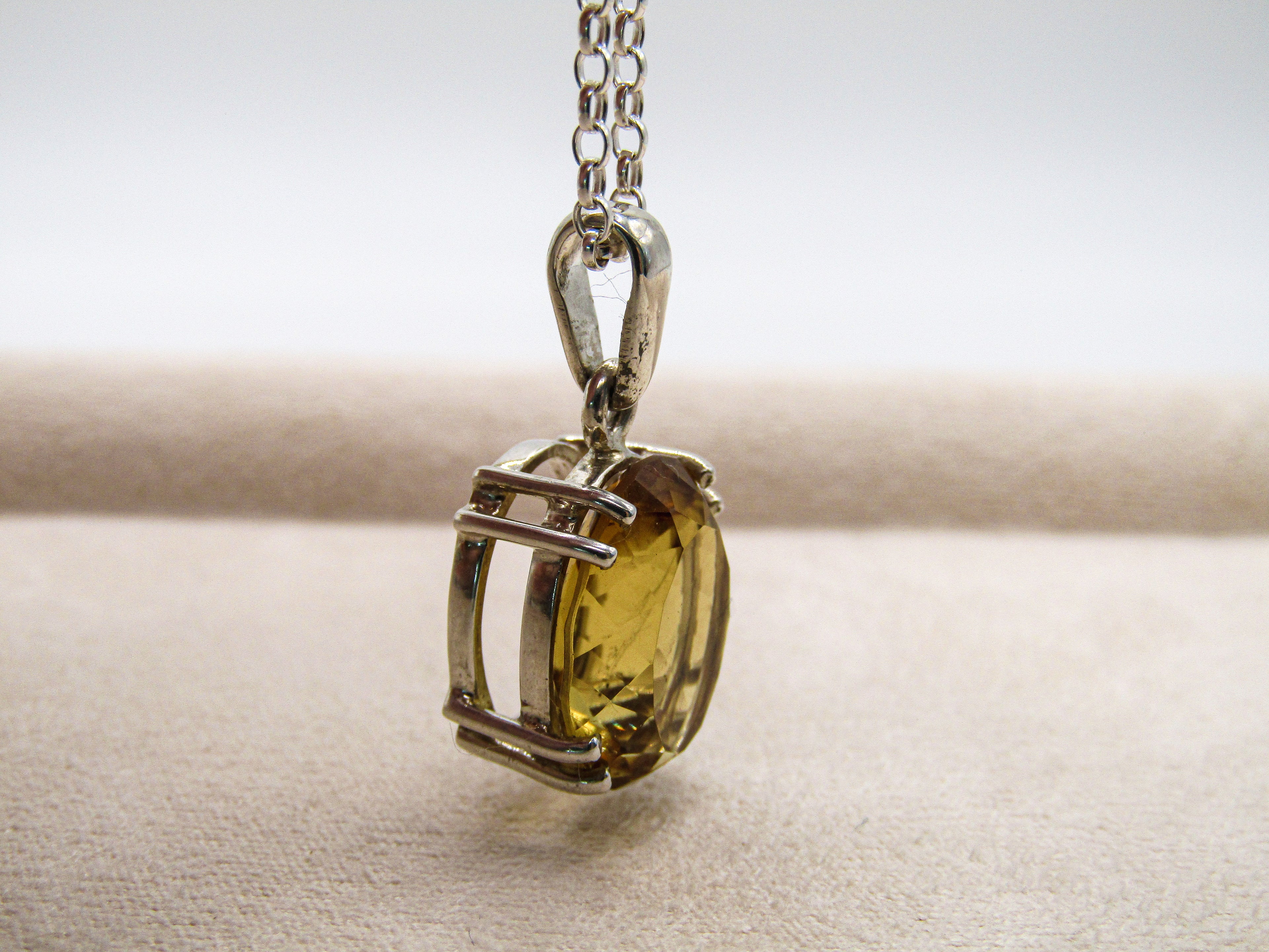Gold pendant with a clear stone on a chain against a neutral background