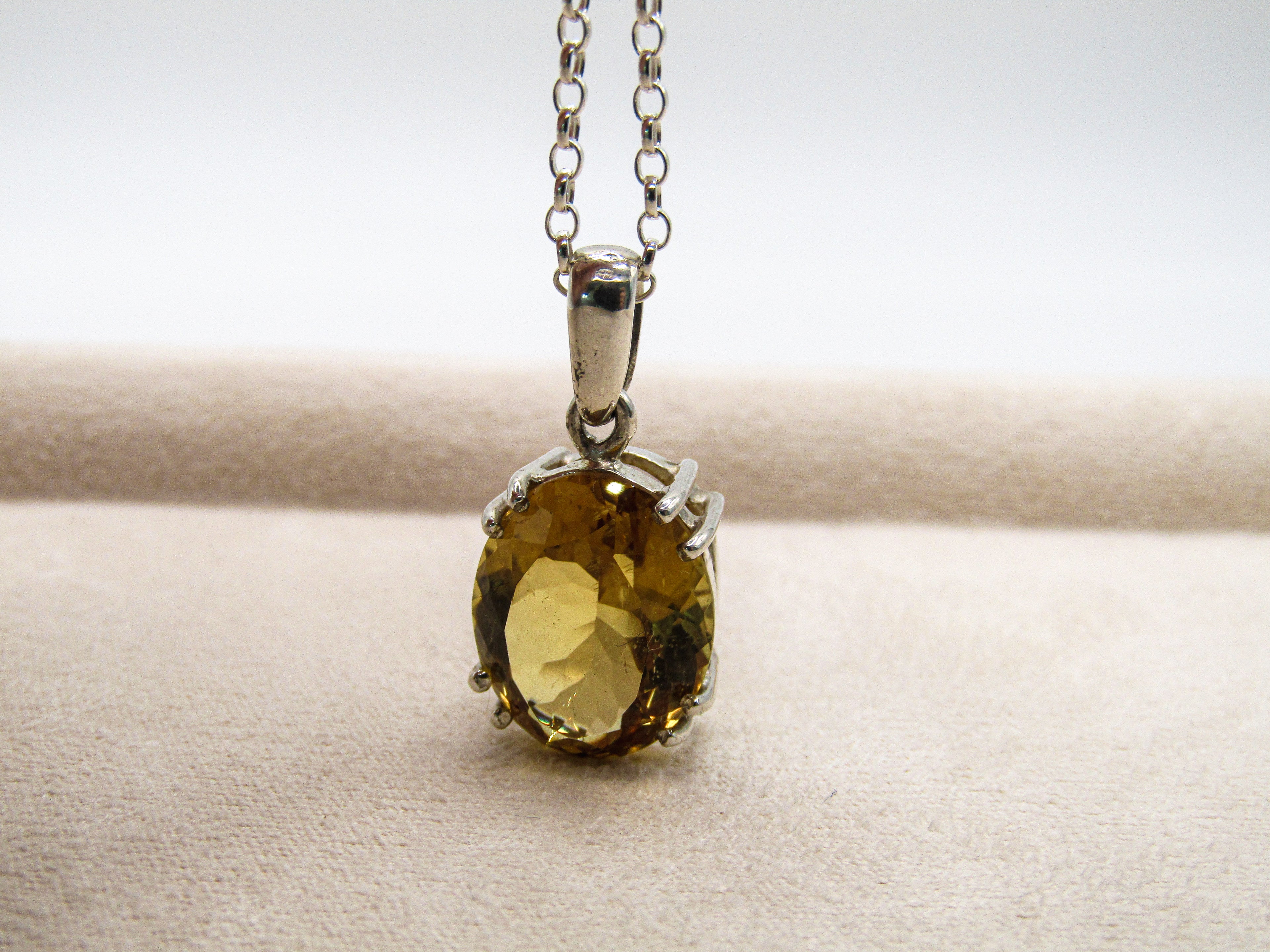 Silver pendant with a yellow gemstone on a neutral background