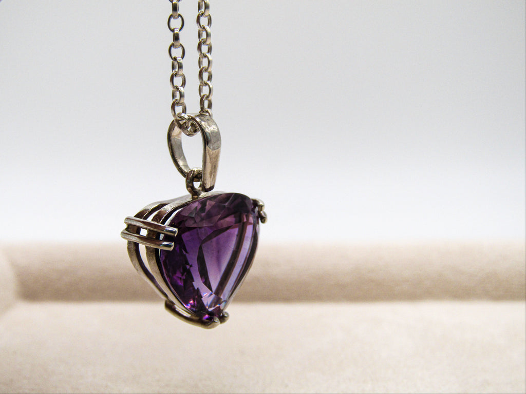 Heart-shaped purple gemstone pendant on a chain against a neutral background