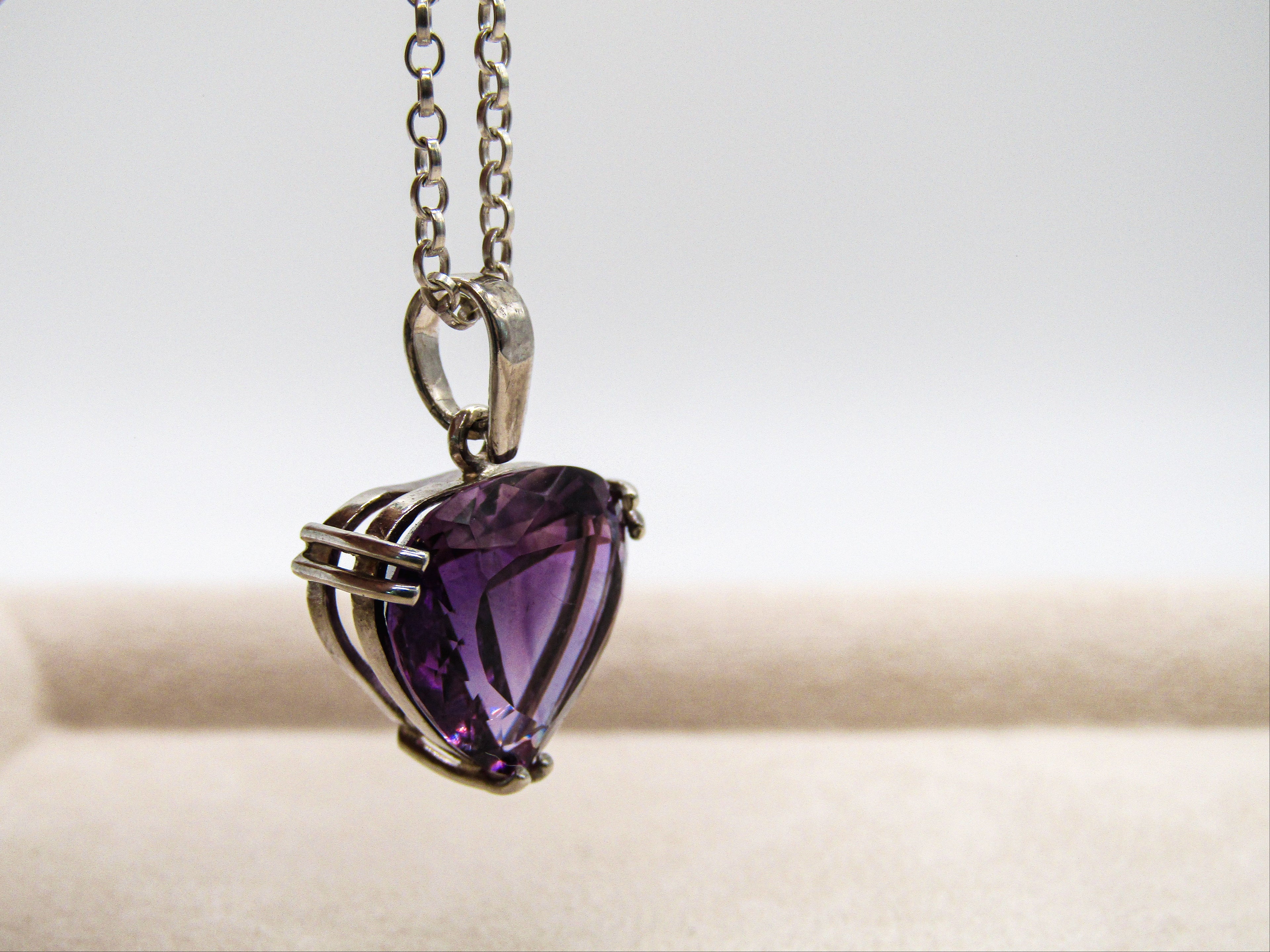 Heart-shaped purple gemstone pendant on a chain against a neutral background