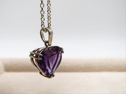 Heart-shaped purple gemstone pendant on a chain against a neutral background