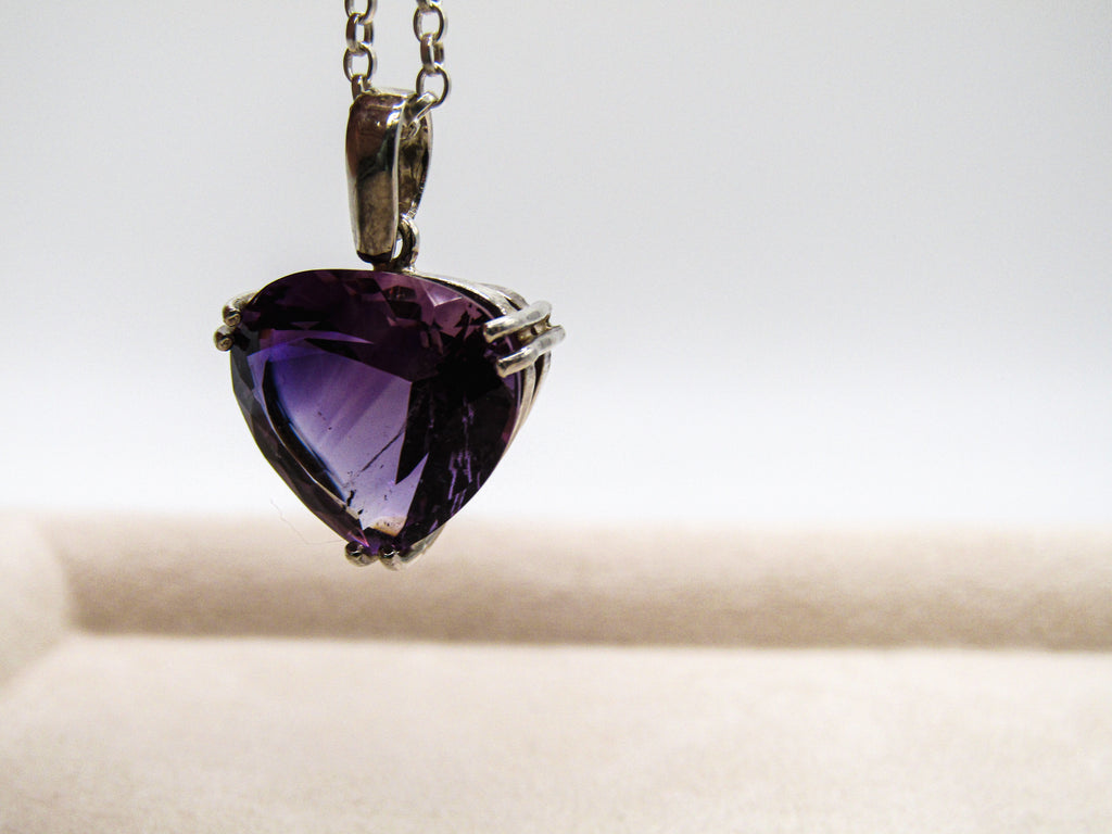 Heart-shaped purple gemstone pendant on a chain against a neutral background