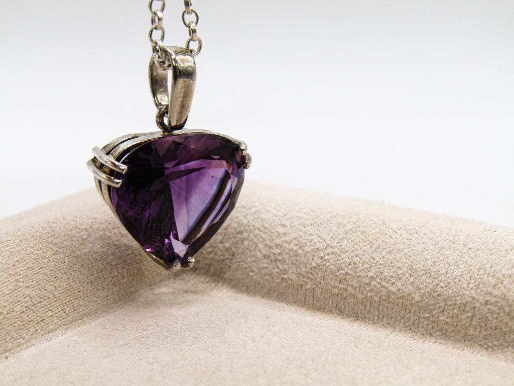 Heart-shaped purple gemstone pendant on a chain against a neutral background