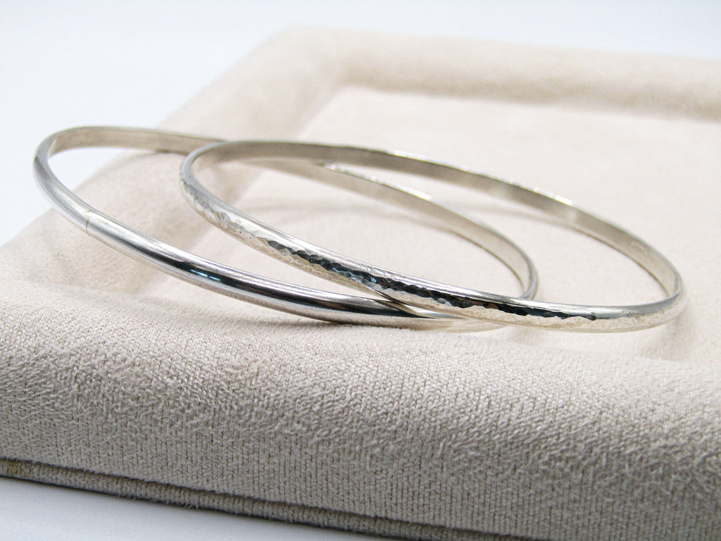 Two silver bangles on a textured beige surface