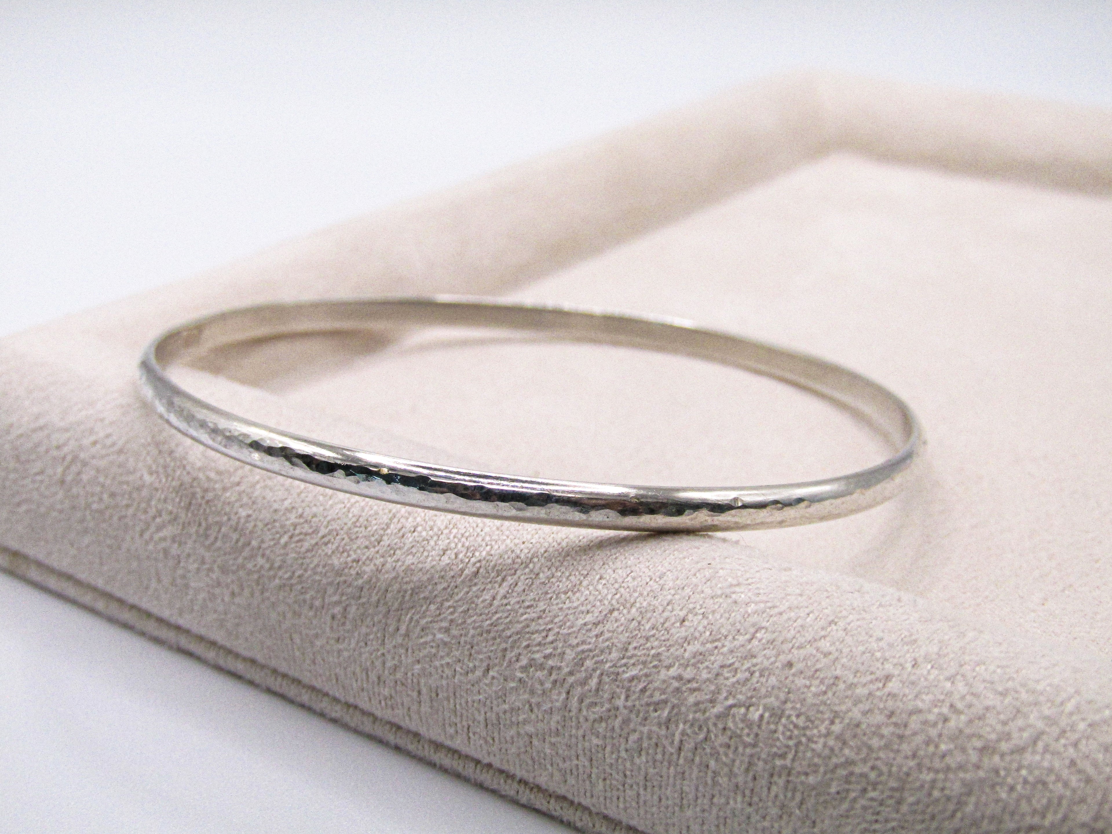 Silver bangle on a textured beige surface