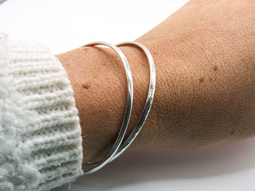 Silver bracelet on a wrist with a white sleeve against a white background