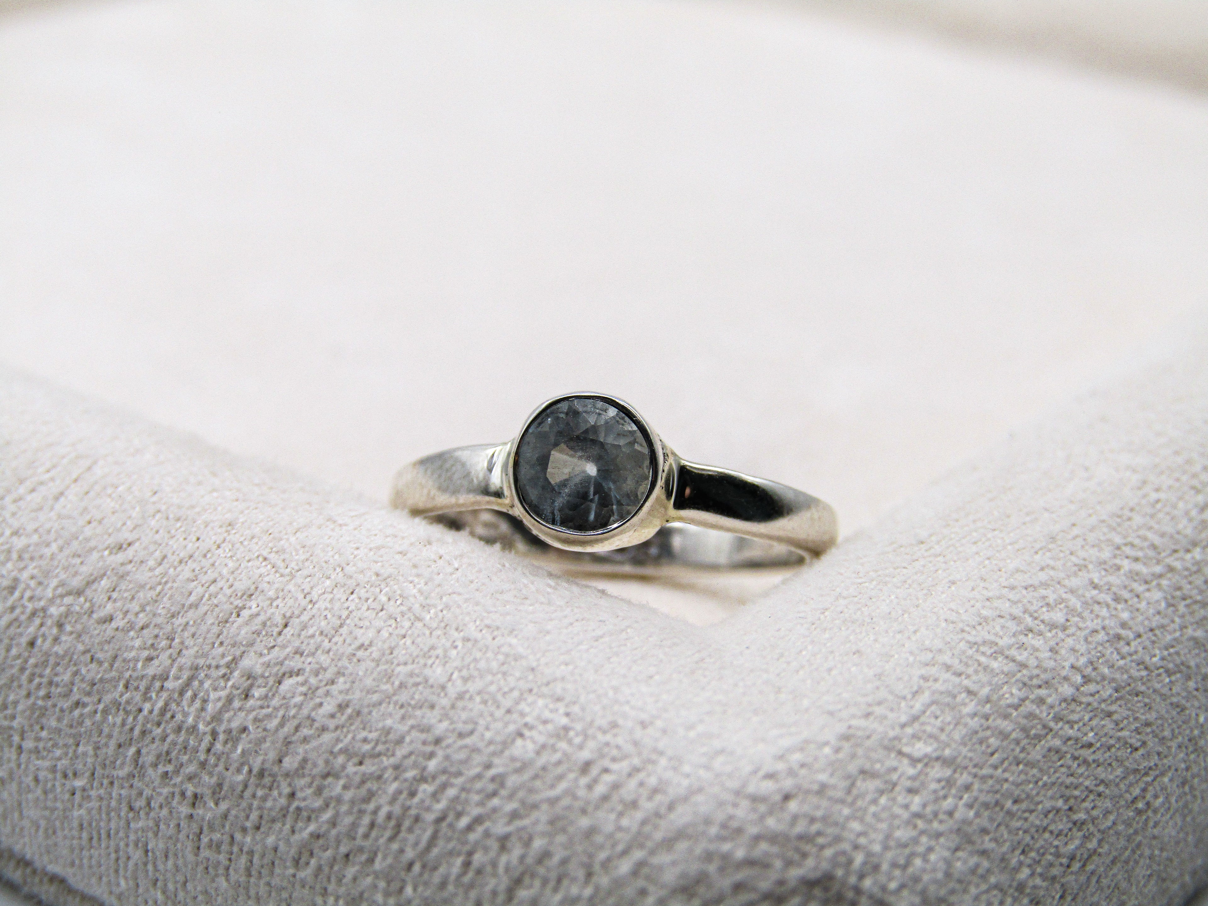 Silver ring with a dark gemstone on a textured white surface