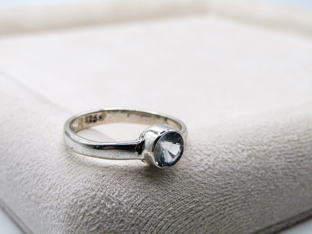 Silver ring with a clear gemstone on a textured beige surface