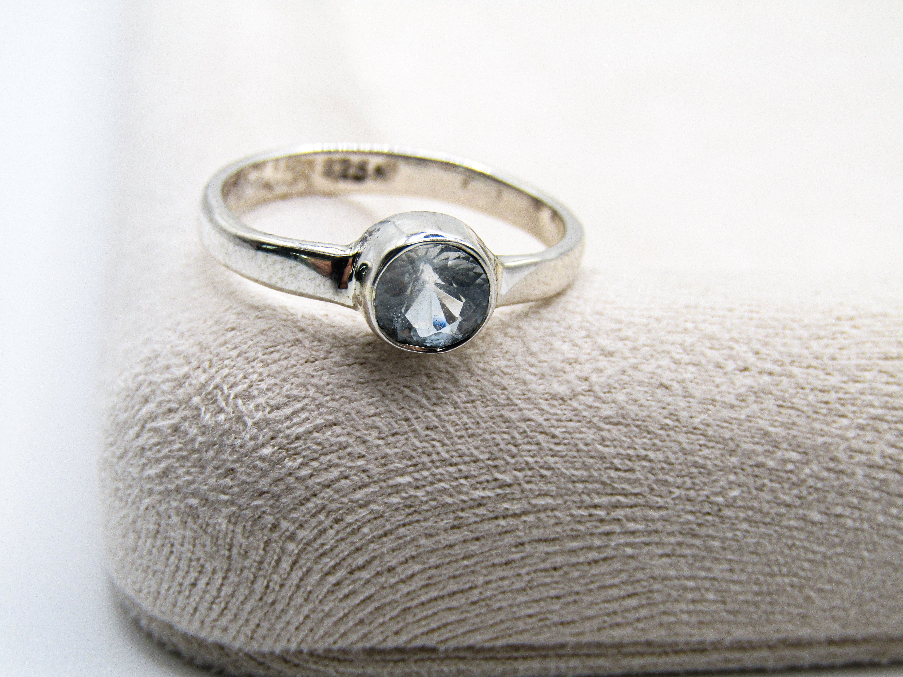 Silver ring with a gemstone on a textured beige surface