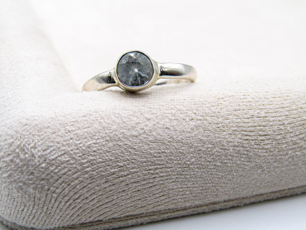Silver ring with a dark gemstone on a textured beige surface