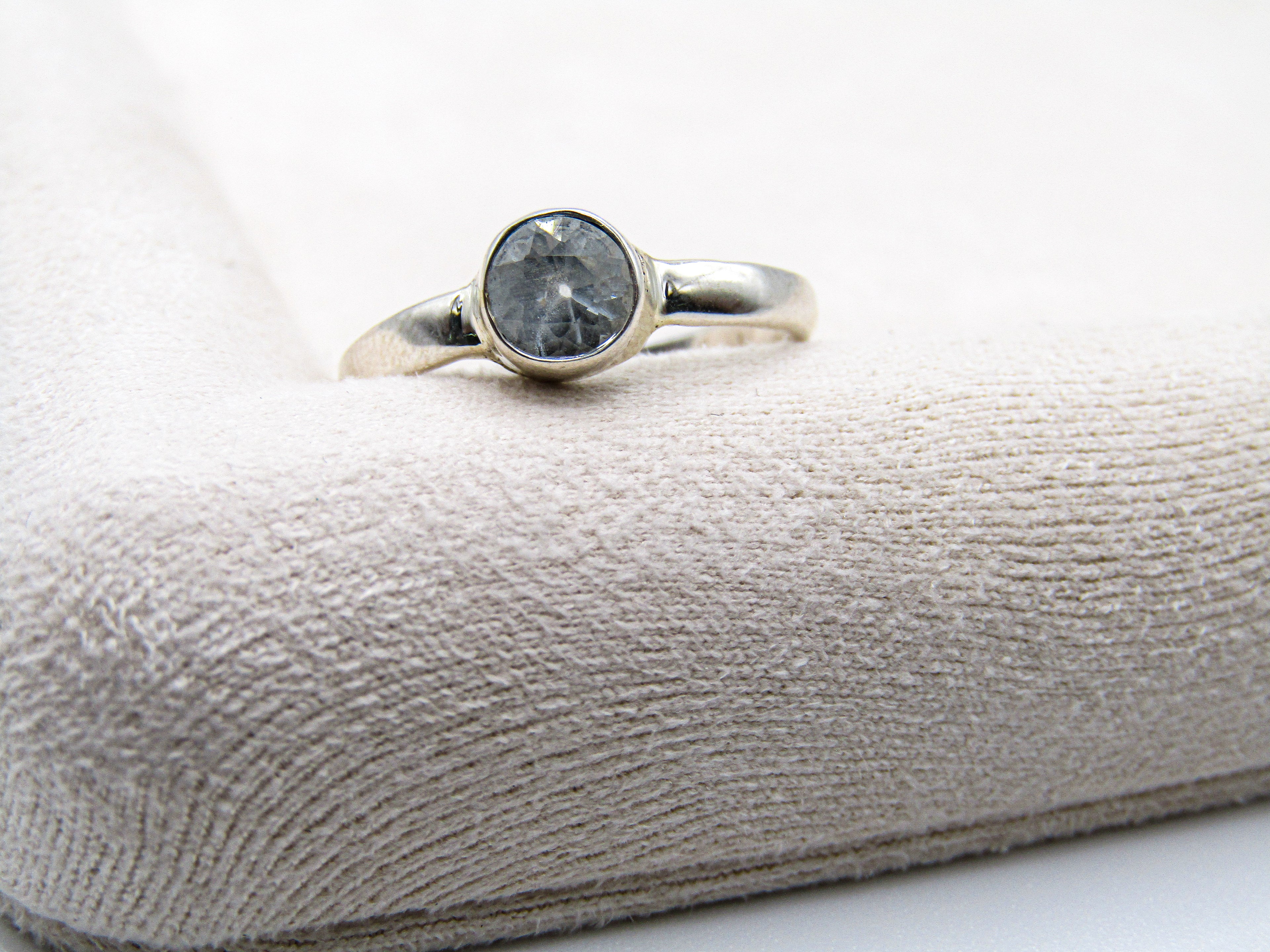 Silver ring with a dark gemstone on a textured beige surface