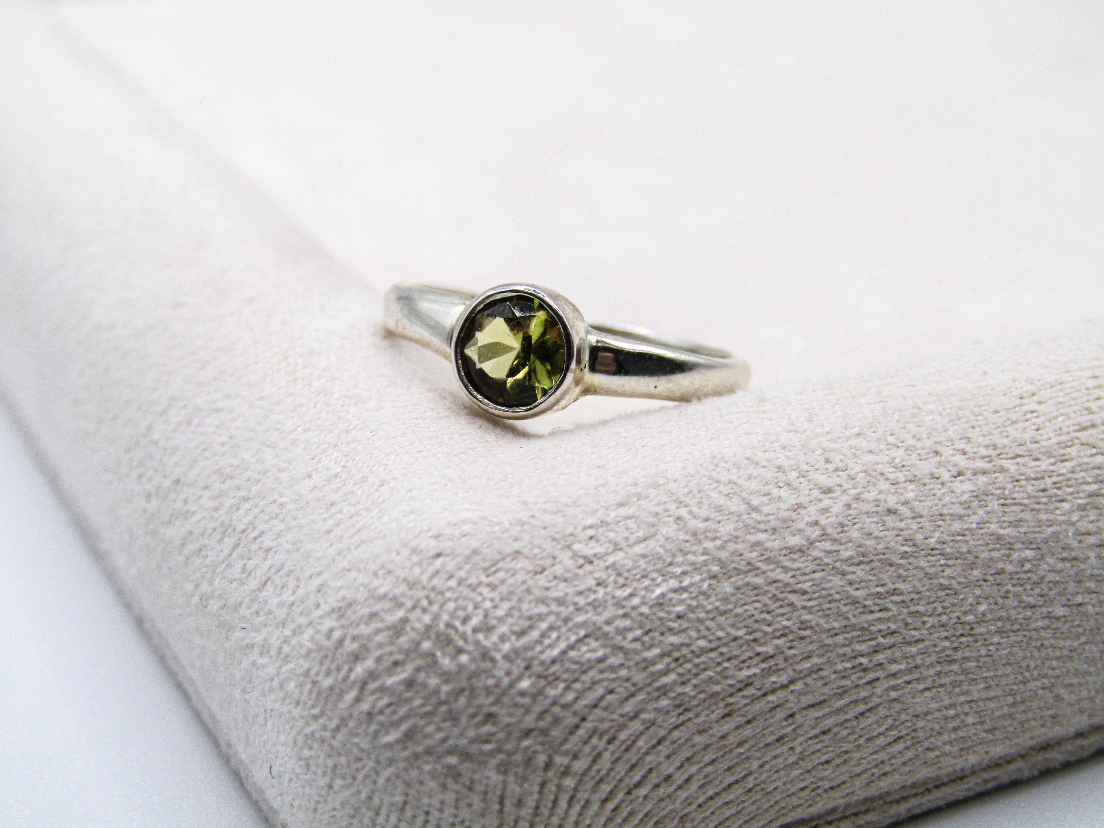 Silver ring with a green gemstone on a textured white surface