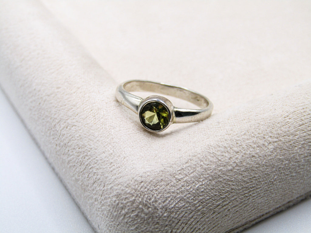 Silver ring with a green gemstone on a textured white surface