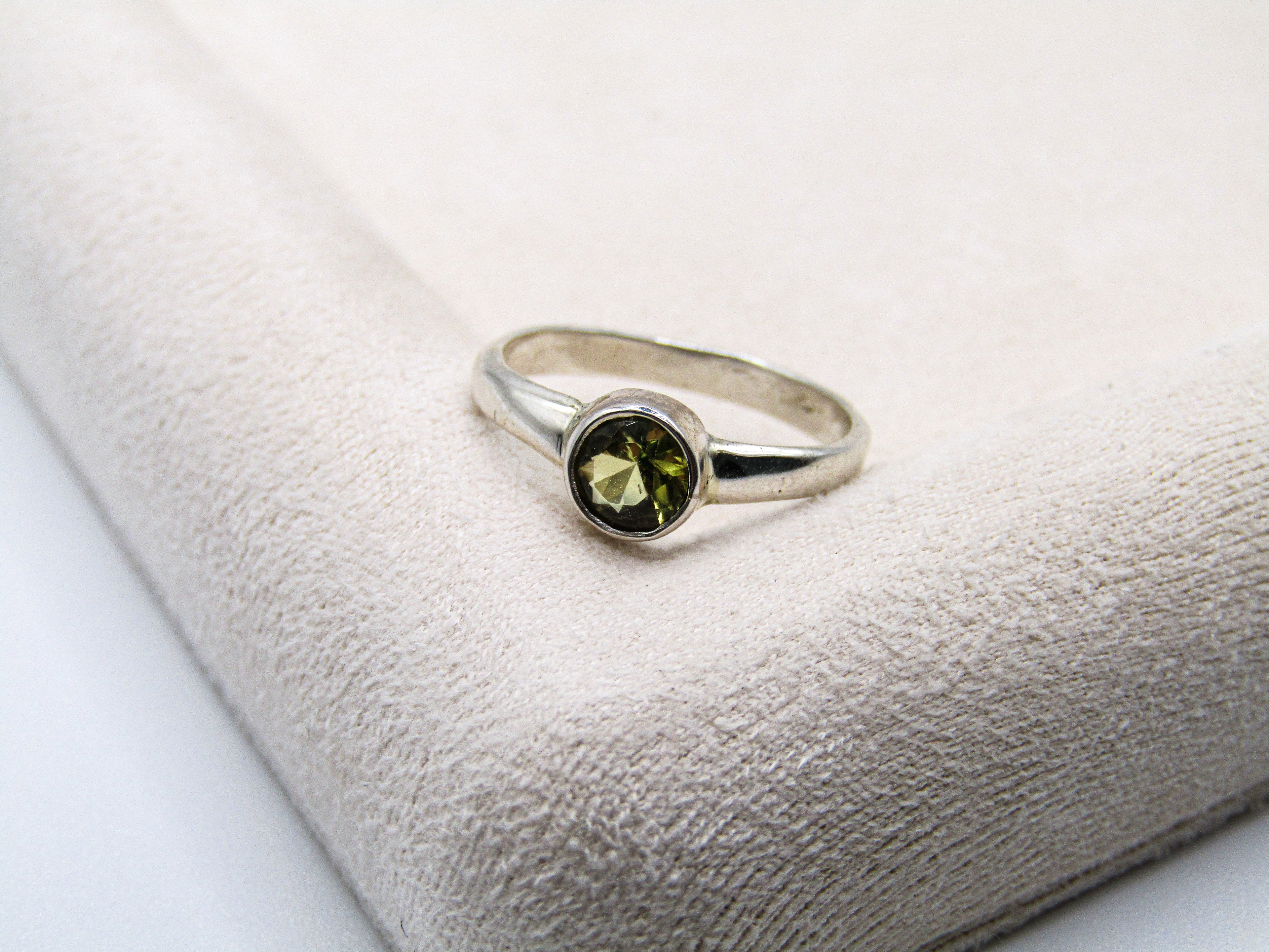 Silver ring with a green gemstone on a textured white surface