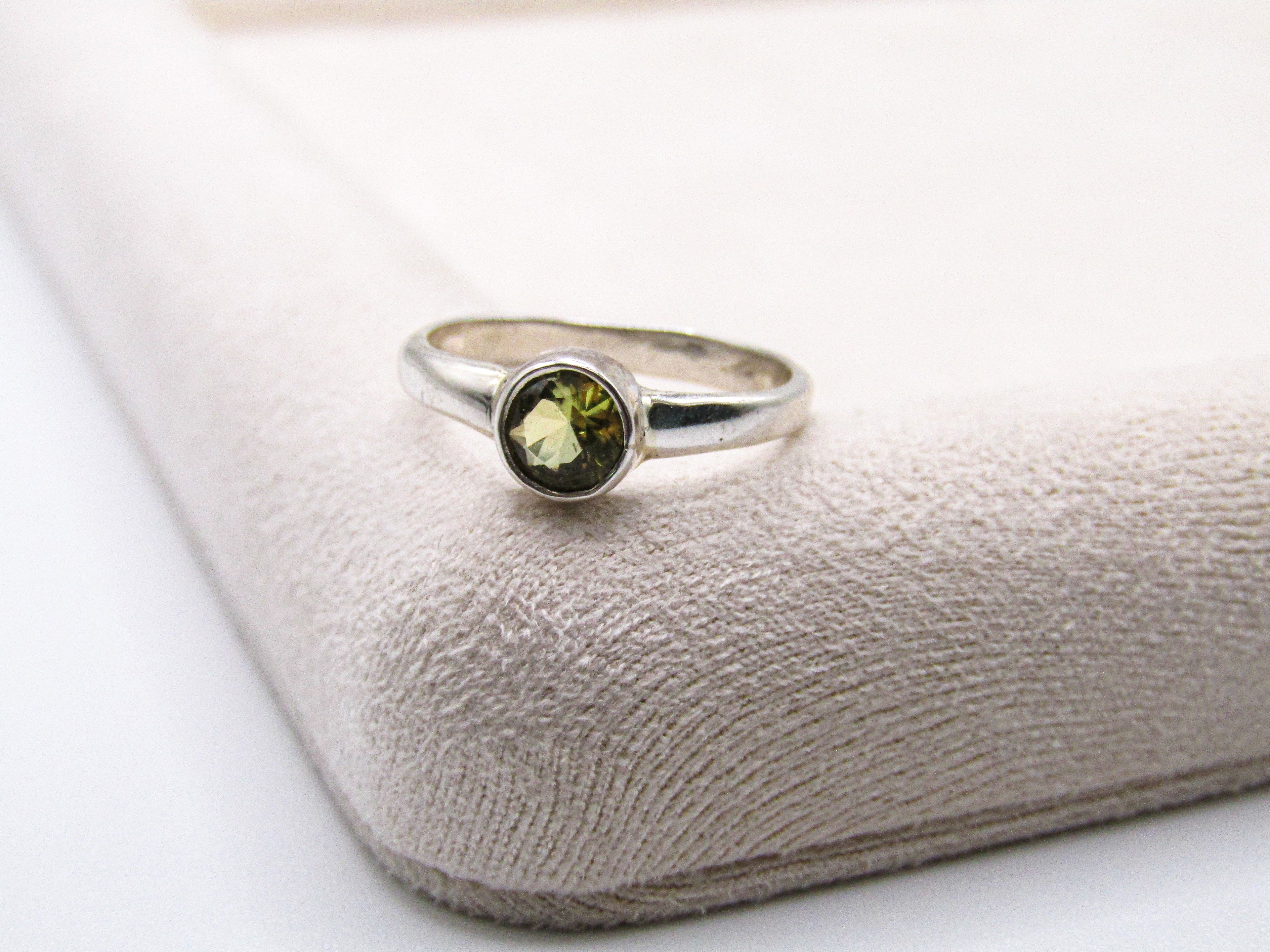 Silver ring with a green gemstone on a textured white surface