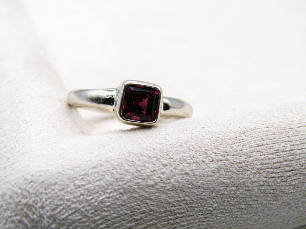 Silver ring with a red gemstone on a textured white surface