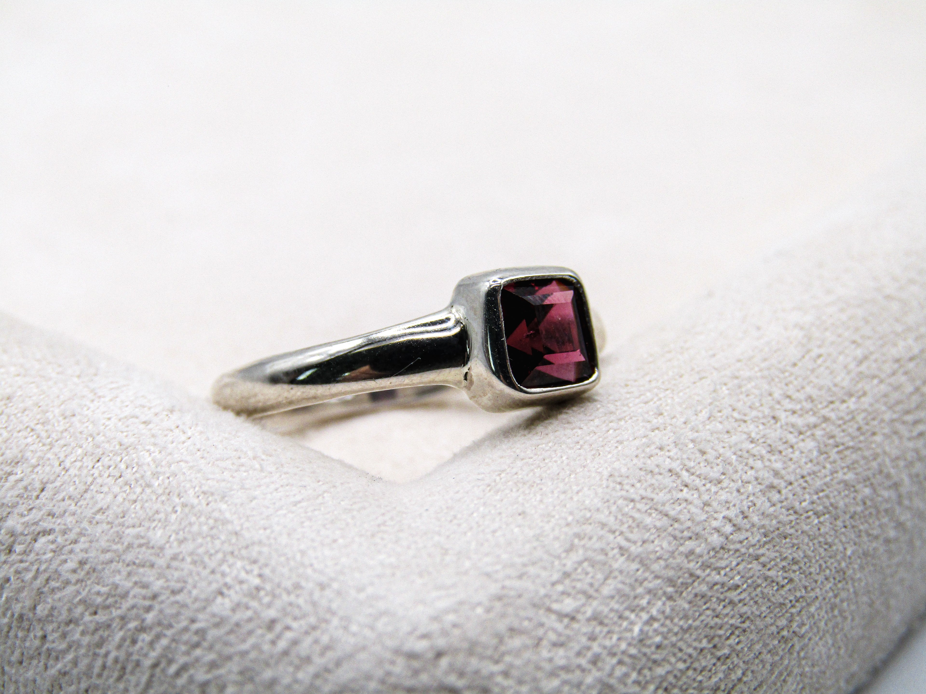 Silver ring with a red gemstone on a white cushion