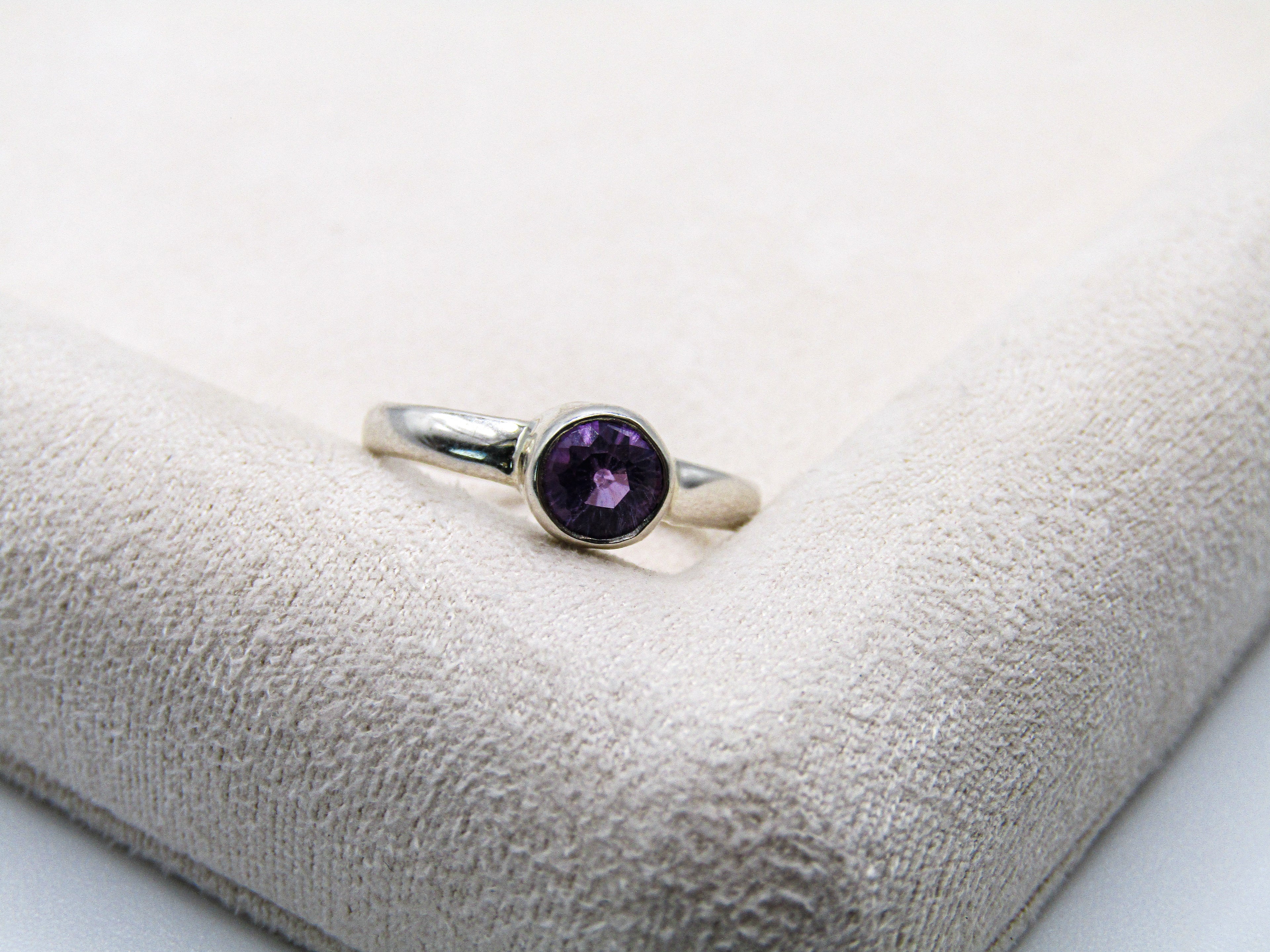 Silver ring with a purple gemstone on a textured white surface