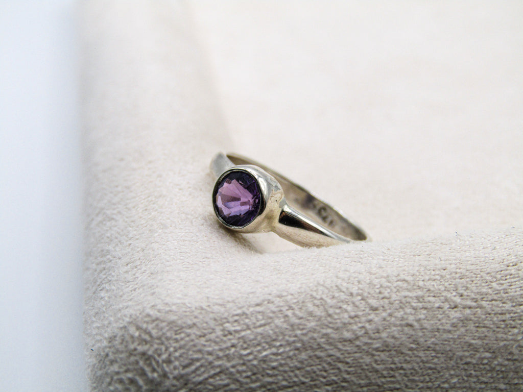 Silver ring with a purple gemstone on a textured white surface