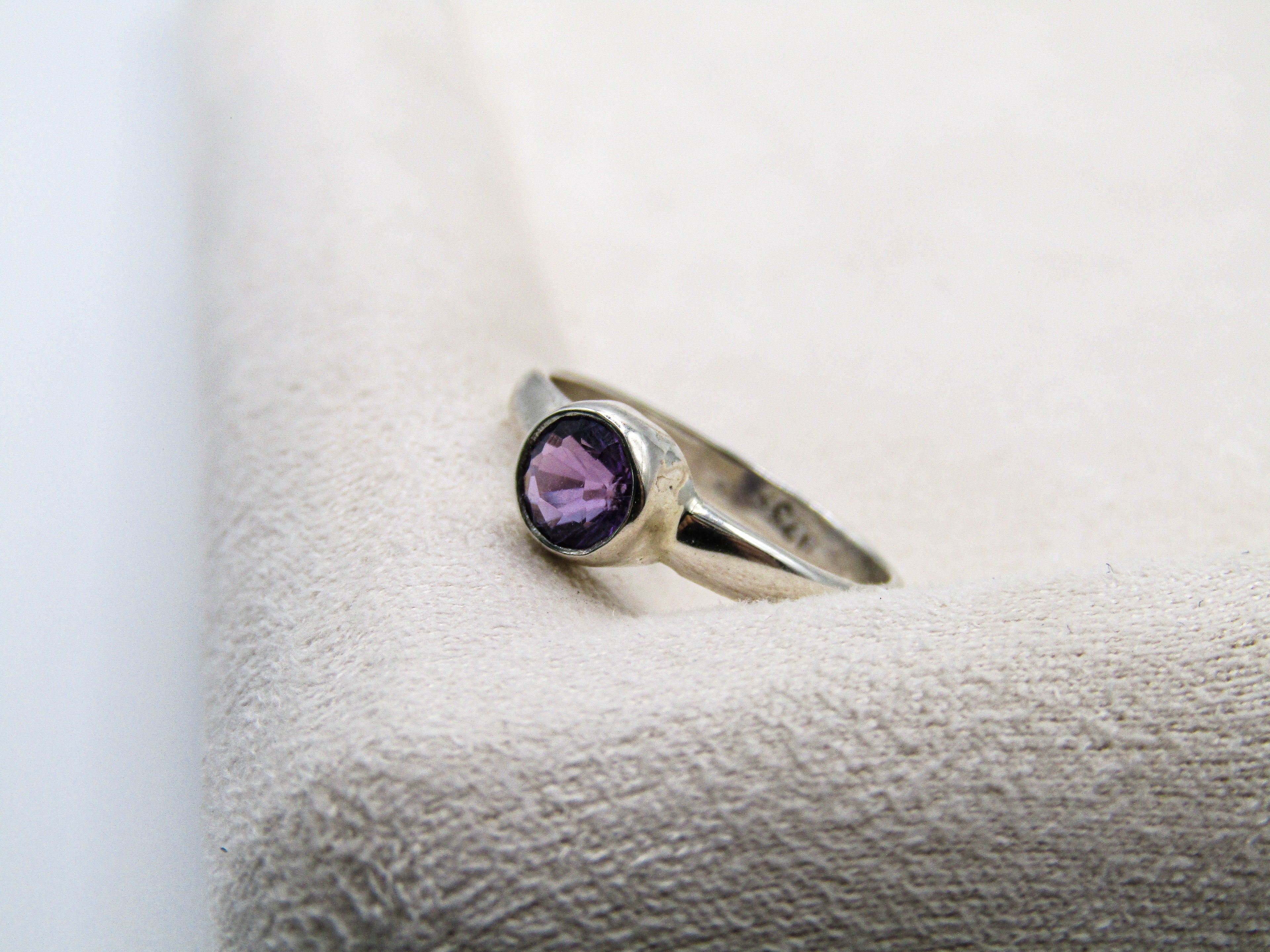 Silver ring with a purple gemstone on a textured white surface