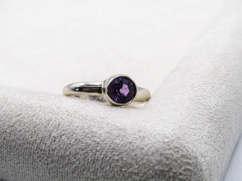 Silver ring with a purple gemstone on a textured white surface