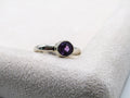 Silver ring with a purple gemstone on a textured white surface