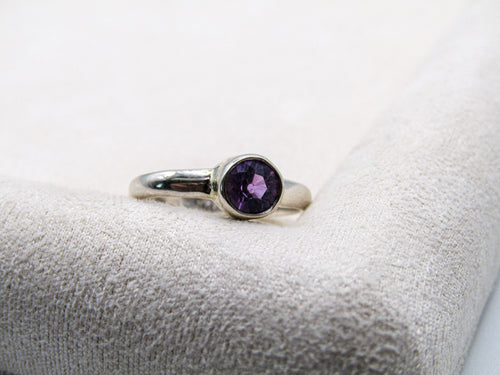 Silver ring with a purple gemstone on a textured white surface