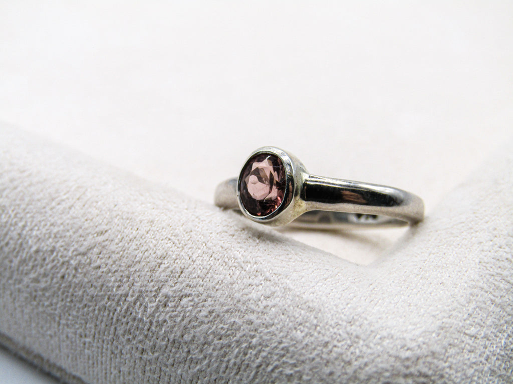 Silver ring with a pink gemstone on a white cushion