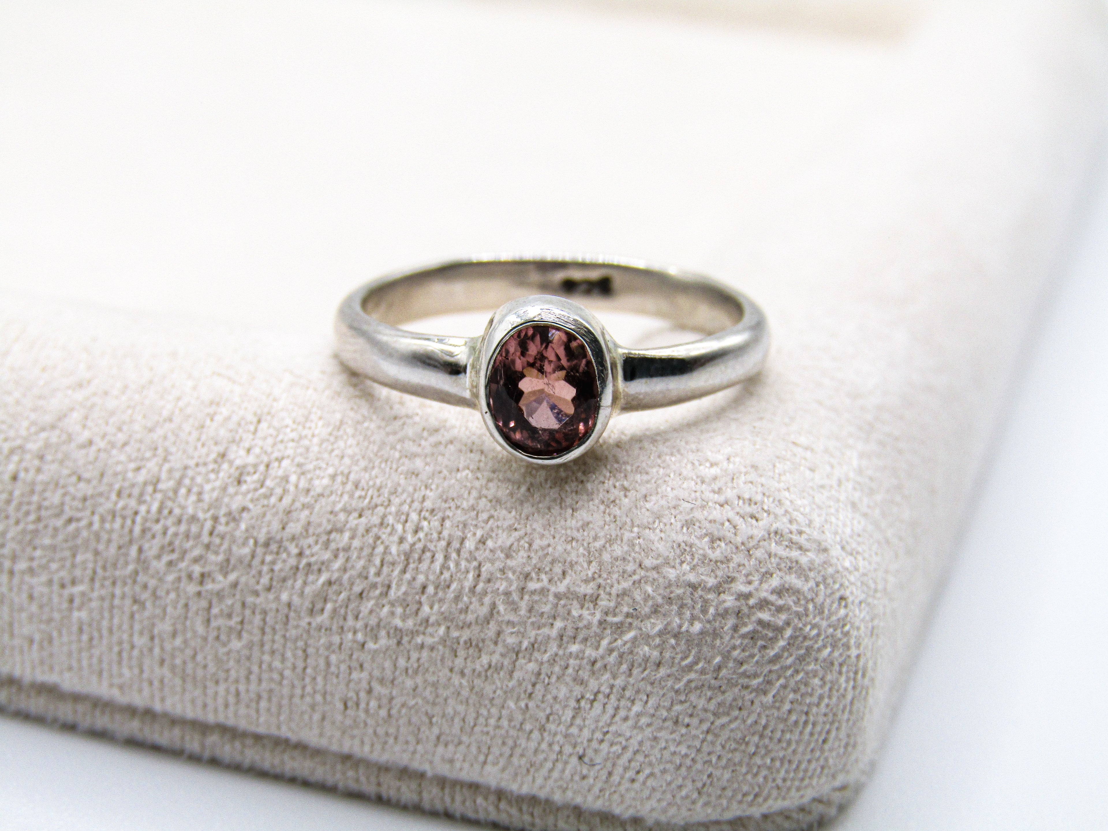 Silver ring with a pink gemstone on a textured beige surface