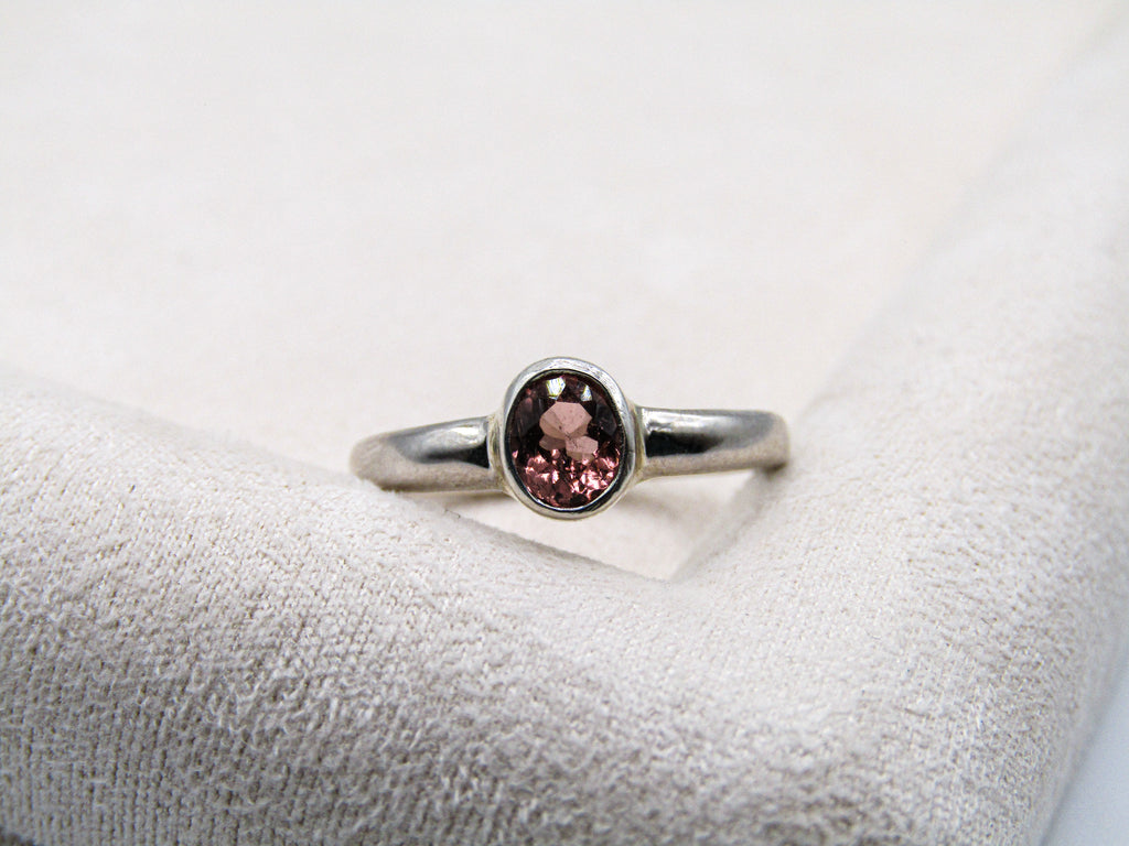 Silver ring with a pink gemstone on a textured white surface