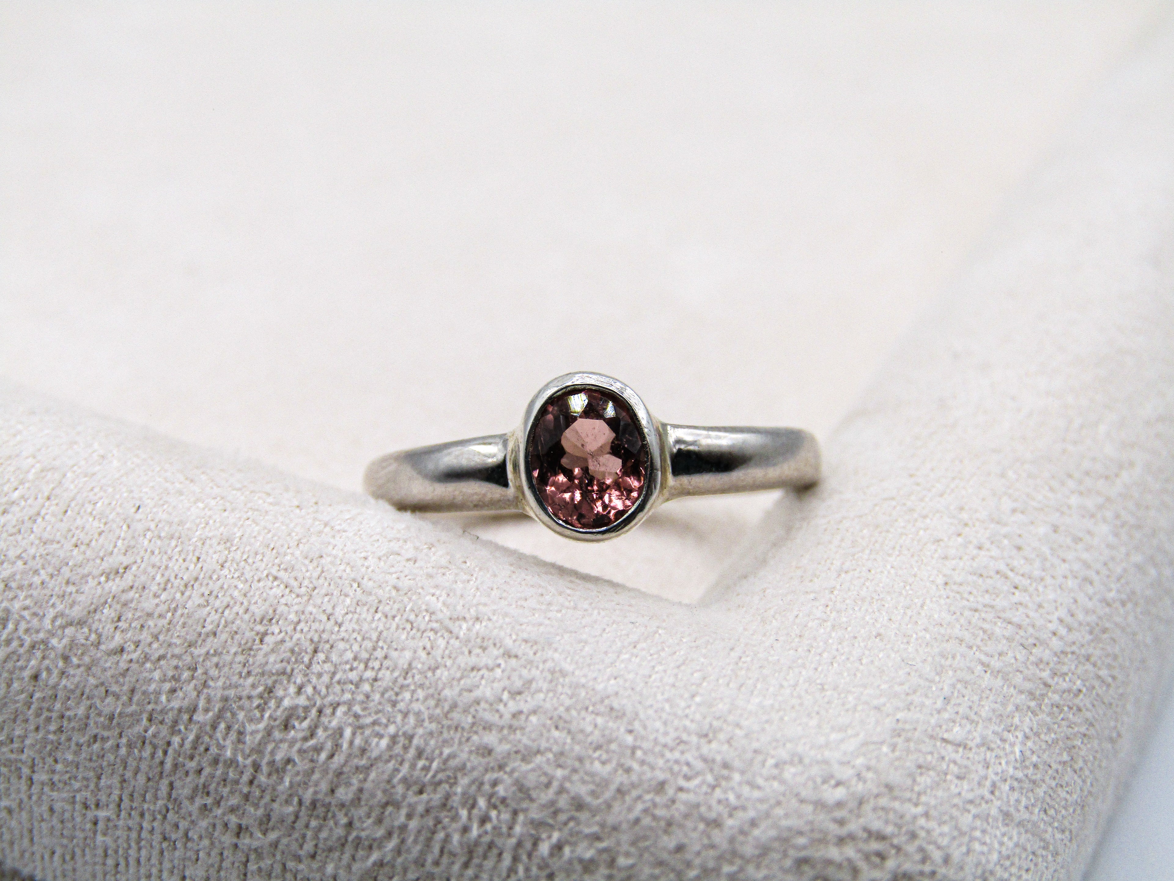 Silver ring with a pink gemstone on a textured white surface