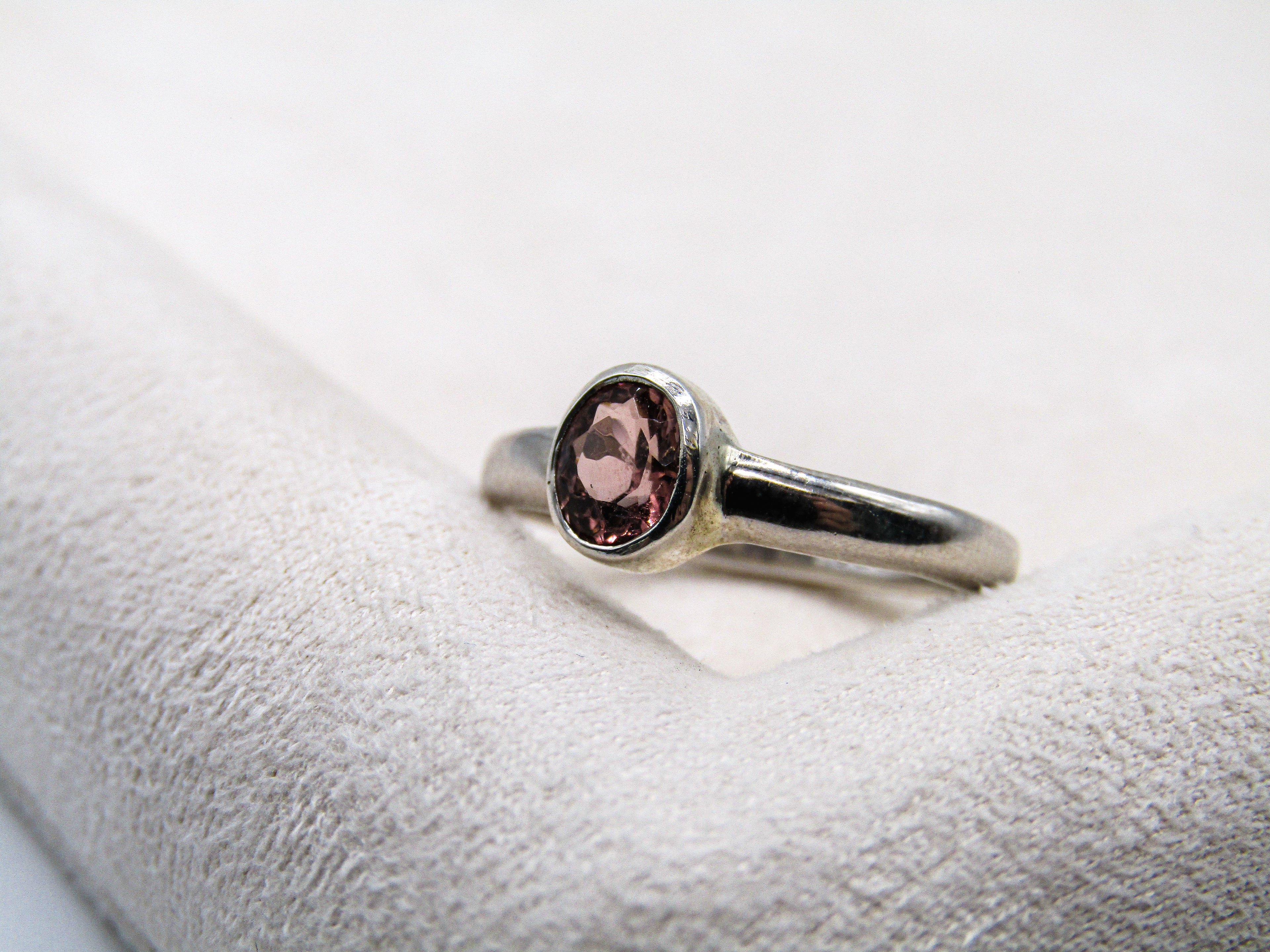 Silver ring with a pink gemstone on a white cushion