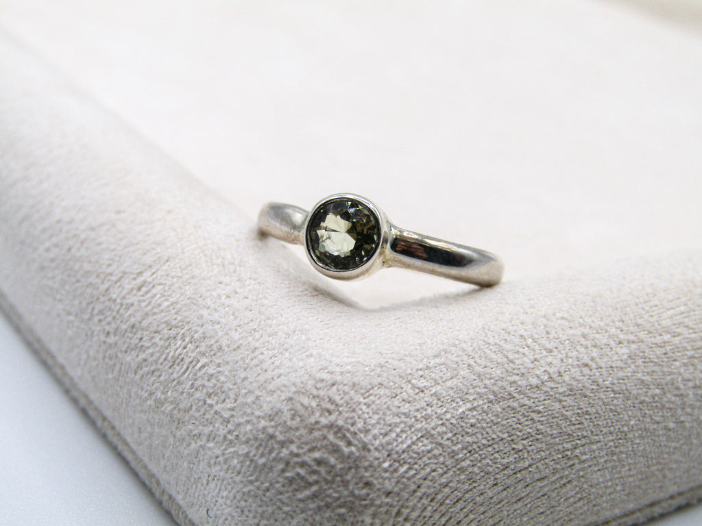 Silver ring with a green gemstone on a textured white surface
