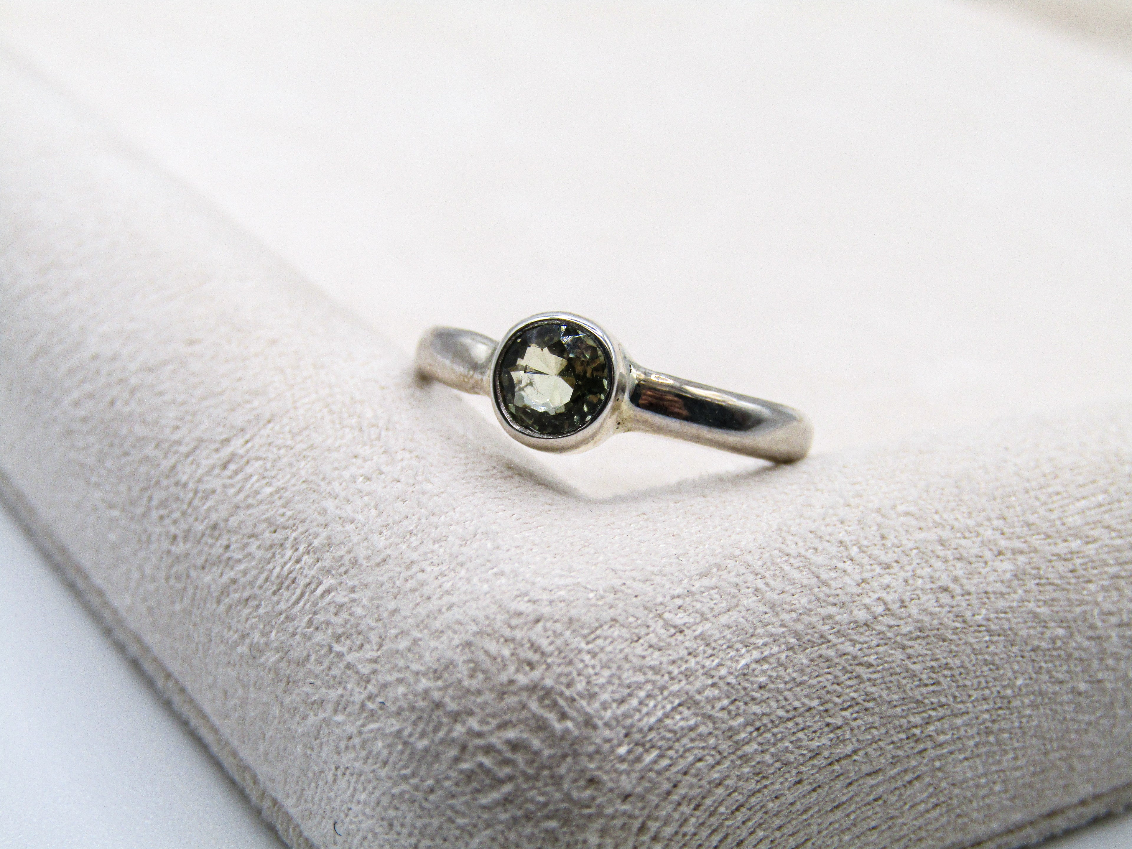 Silver ring with a green gemstone on a textured white surface